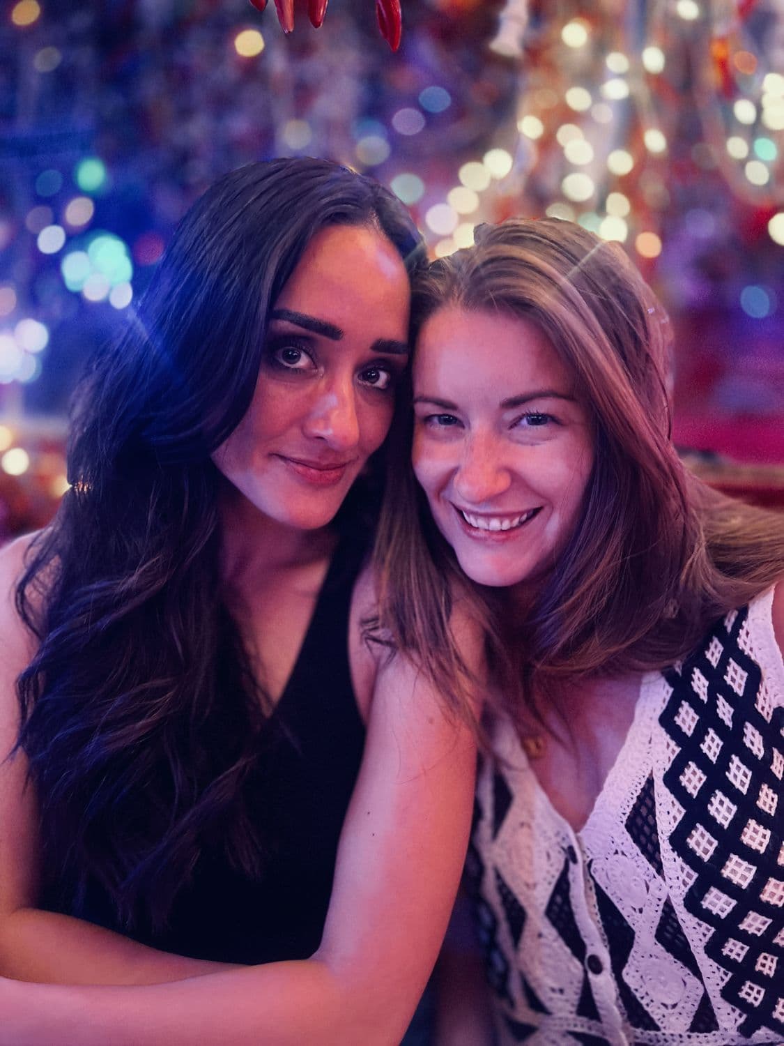 Two friends close together under bokeh party lights